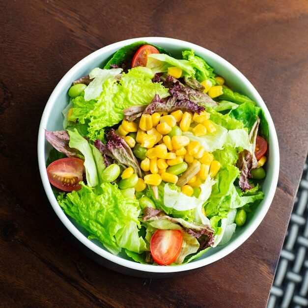 A vibrant salad with lettuce, cherry tomatoes, corn, and edamame in a white bowl.